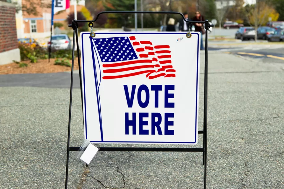 "Vote Here" sidewalk sign with American flag